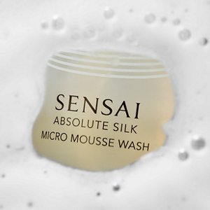 Eine Nahaufnahme des Absolute Silk Micro Mousse Wash, wo die schaumige Textur um die goldene Flasche sichtbar ist